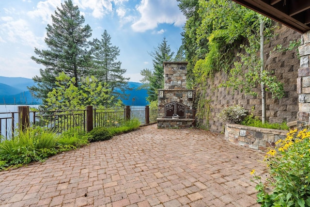 view of patio featuring a mountain view, an outdoor stone fireplace, and fence