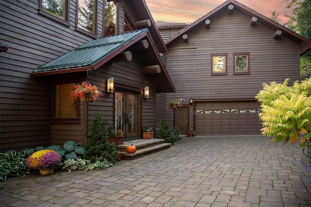 exterior entry at dusk featuring metal roof, decorative driveway, a garage, and french doors