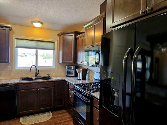 kitchen featuring black appliances, under cabinet range hood, dark wood-style floors, a textured ceiling, and a sink