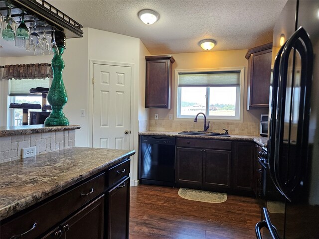 kitchen featuring stone countertops, a sink, black appliances, dark wood-type flooring, and backsplash