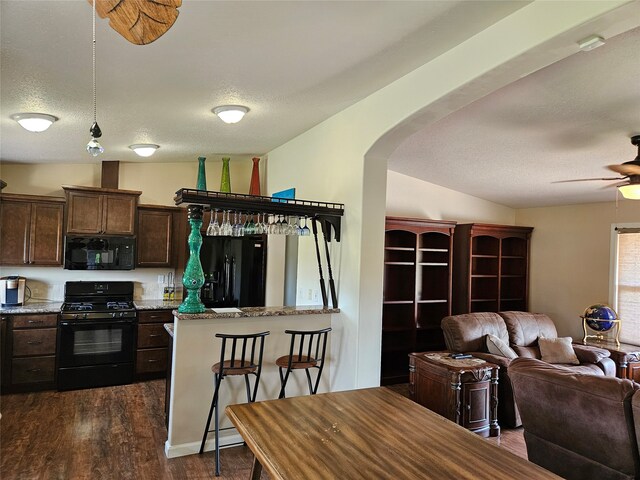 kitchen with black appliances, open floor plan, dark wood finished floors, arched walkways, and dark brown cabinetry