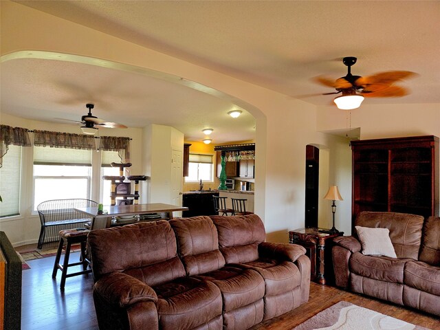 living area with arched walkways, wood finished floors, and a ceiling fan