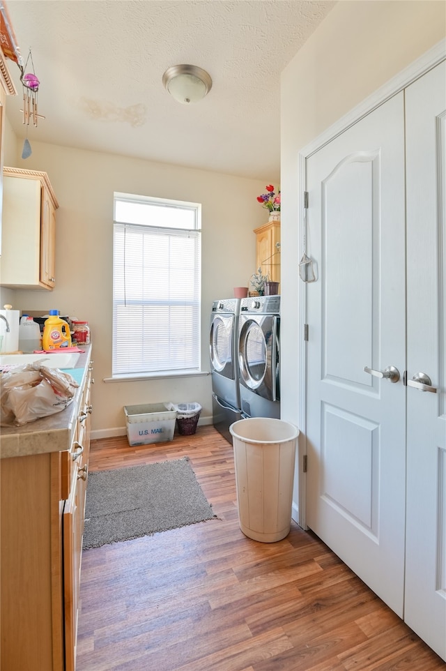 clothes washing area with sink, hardwood / wood-style floors, washer and clothes dryer, and cabinets