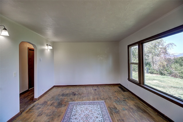 empty room with a textured ceiling, ornamental molding, and hardwood / wood-style floors