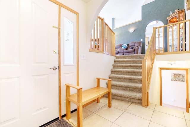 entrance foyer with arched walkways, stairway, and light tile patterned floors