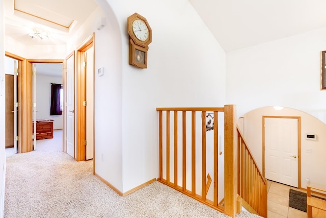 hallway with lofted ceiling, baseboards, arched walkways, and light carpet