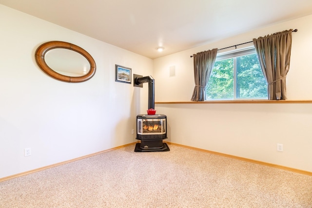 carpeted spare room with a wood stove and baseboards