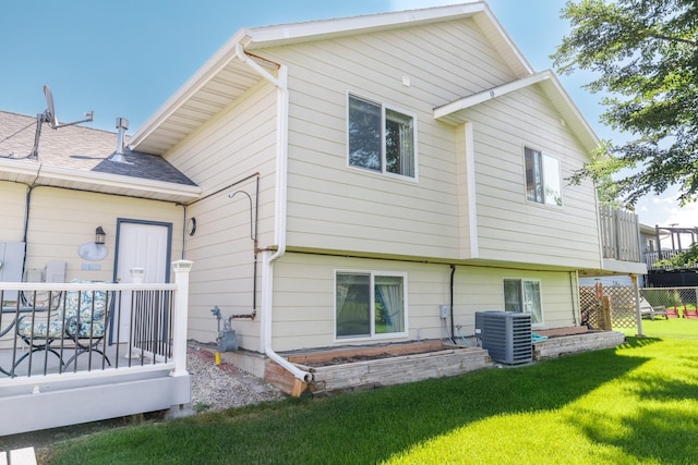 rear view of property with central air condition unit, a shingled roof, and a yard