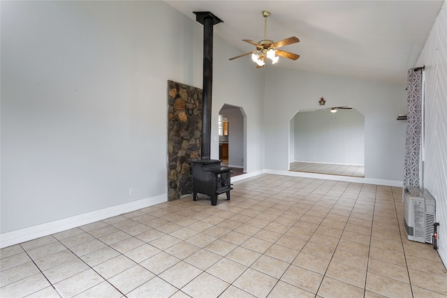 unfurnished living room with arched walkways, light tile patterned floors, a ceiling fan, a wood stove, and high vaulted ceiling