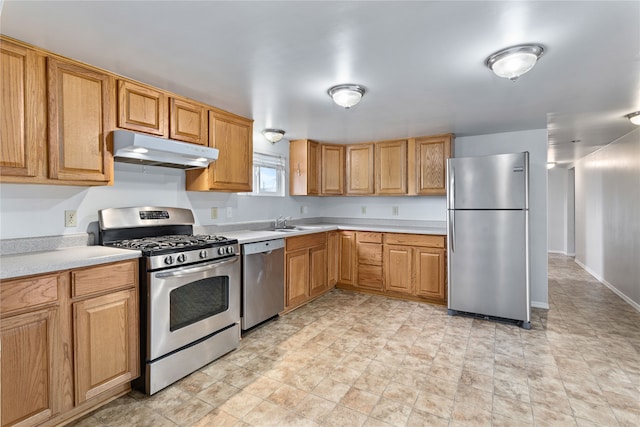 kitchen with baseboards, appliances with stainless steel finishes, light countertops, under cabinet range hood, and a sink