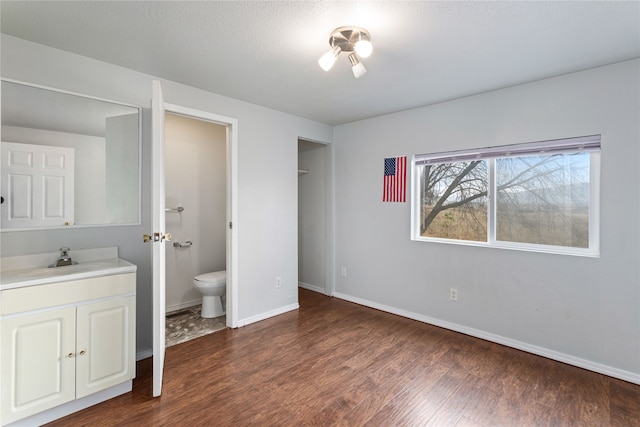 unfurnished bedroom with dark wood-type flooring, connected bathroom, a sink, a textured ceiling, and baseboards