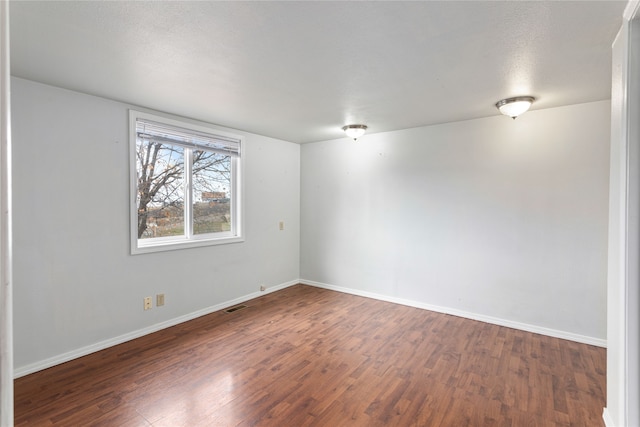 spare room featuring visible vents, baseboards, and dark wood-style flooring