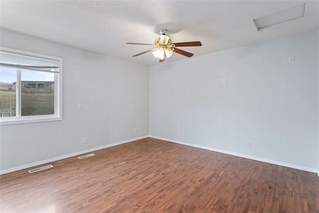 empty room featuring dark wood-style flooring, attic access, visible vents, and baseboards