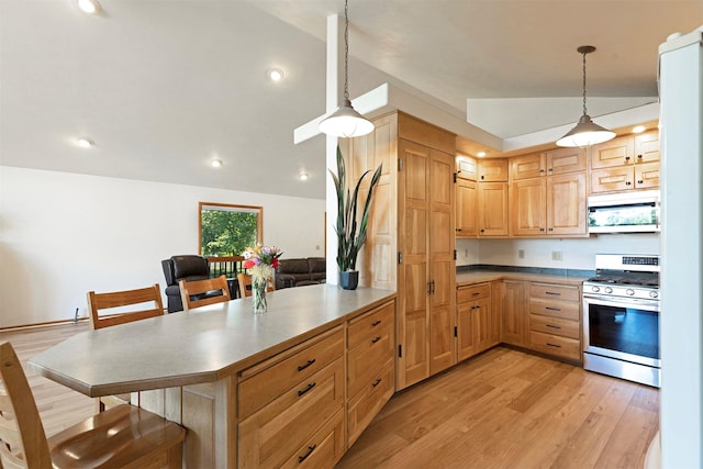 kitchen featuring hanging light fixtures, light brown cabinetry, light wood-style floors, stainless steel gas stove, and a kitchen breakfast bar