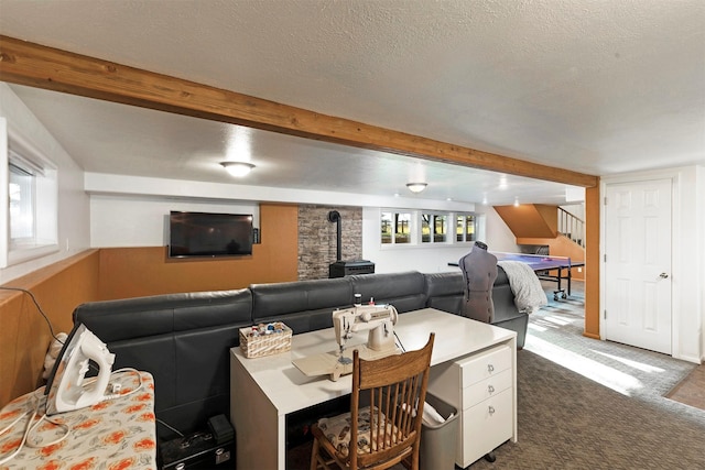 living room featuring beam ceiling, dark colored carpet, stairway, a wood stove, and a textured ceiling