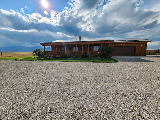 view of front facade with gravel driveway, covered porch, metal roof, fence, and a garage