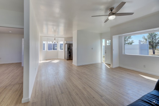 unfurnished living room with light hardwood / wood-style floors, a wealth of natural light, and ceiling fan with notable chandelier