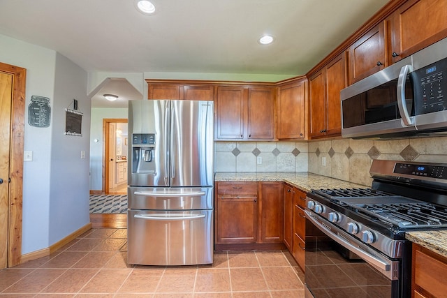 kitchen featuring appliances with stainless steel finishes, light tile patterned floors, tasteful backsplash, and light stone countertops