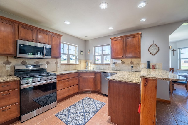 kitchen with kitchen peninsula, stainless steel appliances, plenty of natural light, sink, and a breakfast bar area