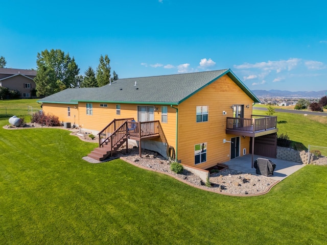 rear view of house with a deck with mountain view, a patio, central AC unit, and a yard