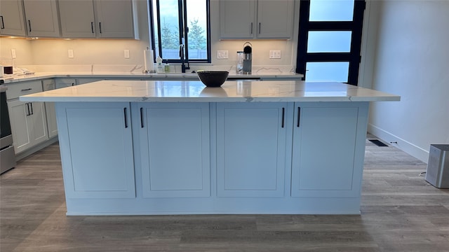 kitchen featuring a kitchen island, light hardwood / wood-style flooring, sink, and light stone counters