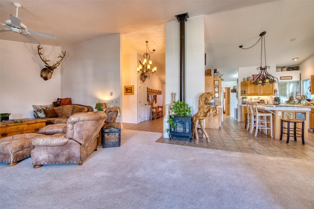 living area with ceiling fan with notable chandelier, a wood stove, light tile patterned floors, and light colored carpet