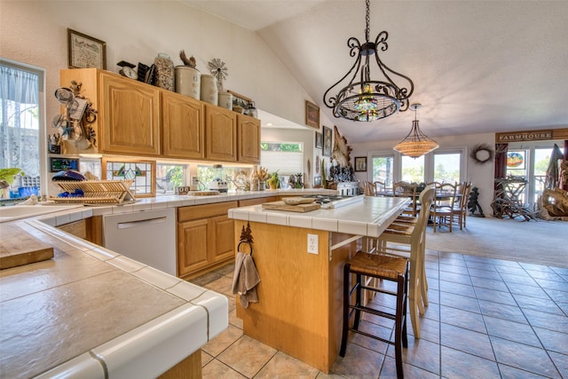 kitchen with light tile patterned floors, lofted ceiling, tile counters, dishwasher, and a center island