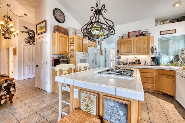 kitchen with a notable chandelier, a kitchen island, white appliances, light tile patterned floors, and tile counters