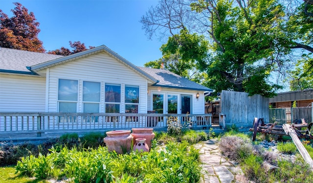 back of property with fence, a deck, and a shingled roof