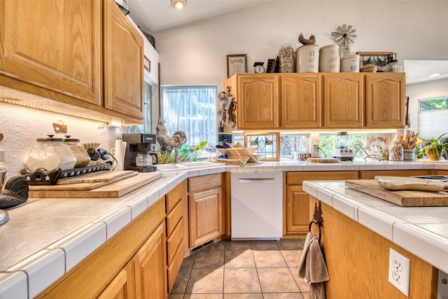 kitchen featuring dishwasher, vaulted ceiling, tile countertops, and light tile patterned floors