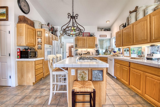 kitchen featuring white appliances, a kitchen island, light tile patterned flooring, tile counters, and vaulted ceiling