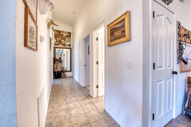 hallway with light tile patterned floors, baseboards, visible vents, lofted ceiling, and a textured wall