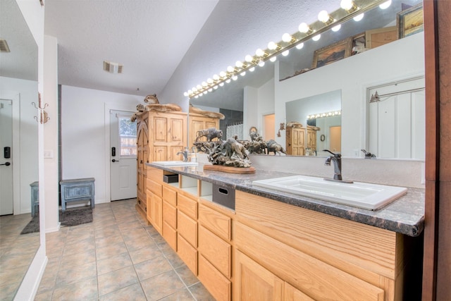 bathroom with visible vents, a sink, a textured ceiling, tile patterned flooring, and lofted ceiling