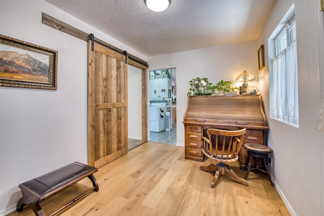 office space featuring baseboards, wood finished floors, a barn door, a textured wall, and a textured ceiling