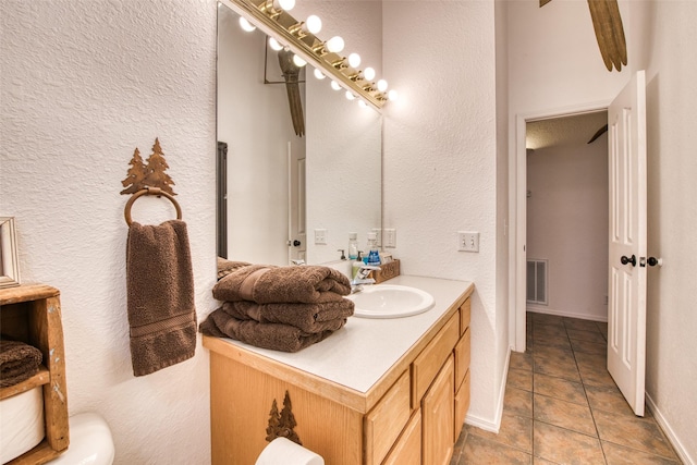 bathroom with tile patterned floors, visible vents, baseboards, vanity, and a textured wall