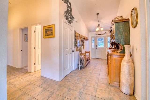 foyer entrance featuring light tile patterned floors, a notable chandelier, high vaulted ceiling, and baseboards