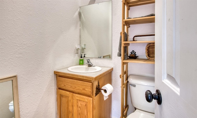 bathroom featuring toilet, vanity, and a textured wall