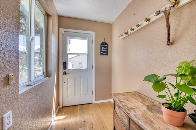 doorway to outside featuring light wood-style flooring, a textured ceiling, baseboards, and a textured wall