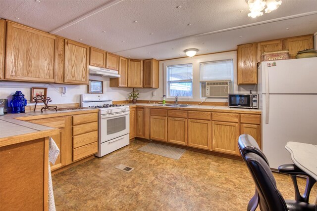 kitchen featuring visible vents, tile counters, under cabinet range hood, white appliances, and a sink