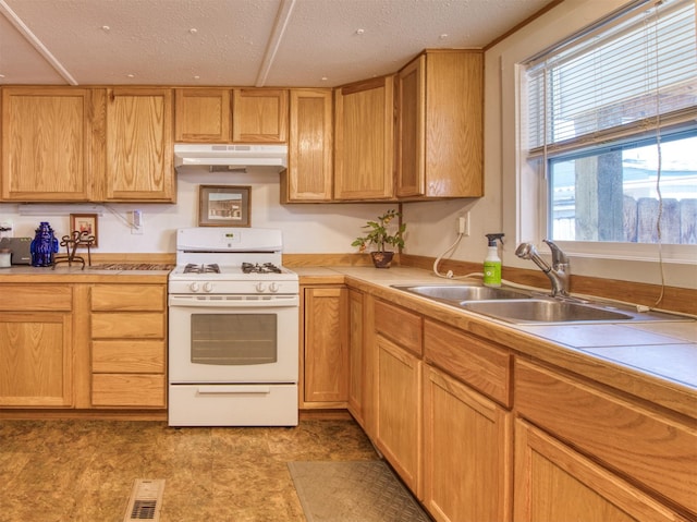 kitchen with under cabinet range hood, light countertops, white gas range, a textured ceiling, and a sink