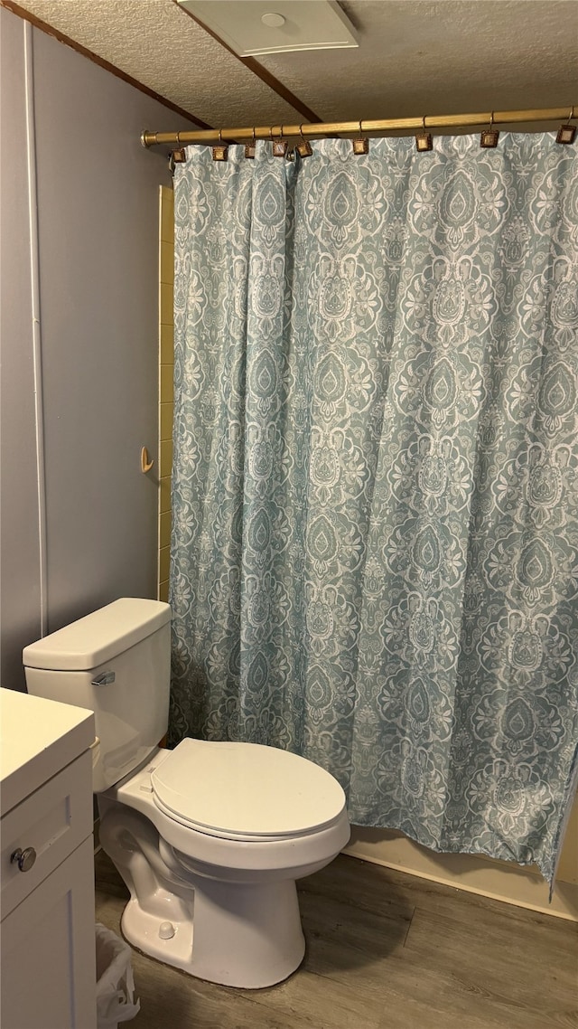 bathroom featuring hardwood / wood-style flooring, a textured ceiling, walk in shower, toilet, and vanity