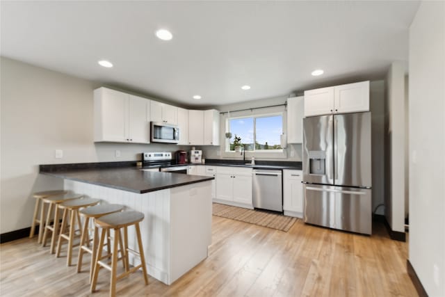 kitchen featuring appliances with stainless steel finishes, kitchen peninsula, light hardwood / wood-style flooring, and white cabinets