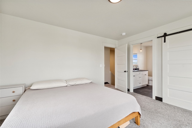 bedroom with a barn door, dark carpet, sink, and ensuite bathroom