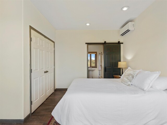 bedroom featuring a barn door, a closet, dark hardwood / wood-style flooring, and a wall unit AC