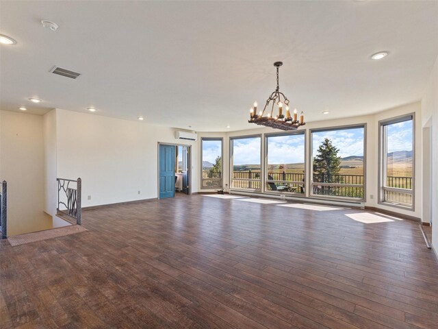 unfurnished living room with dark wood-type flooring, an inviting chandelier, and an AC wall unit