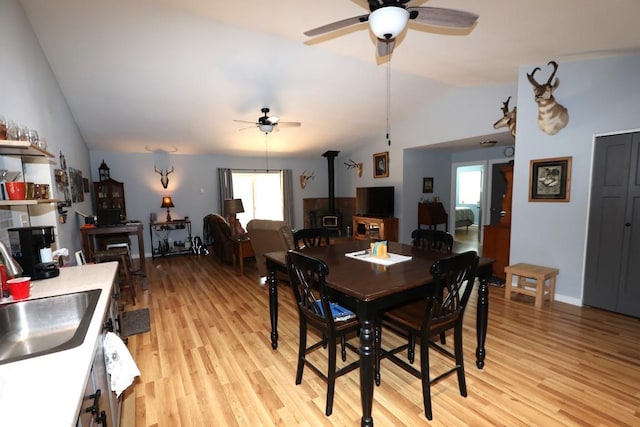 dining room with light wood-style floors, a wood stove, vaulted ceiling, and ceiling fan