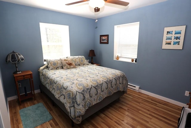 bedroom with baseboards, multiple windows, a baseboard heating unit, and wood finished floors