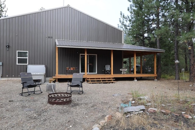 rear view of house with covered porch, metal roof, an outdoor fire pit, and board and batten siding