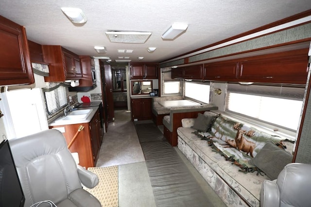 kitchen with reddish brown cabinets, visible vents, stainless steel microwave, a sink, and a textured ceiling