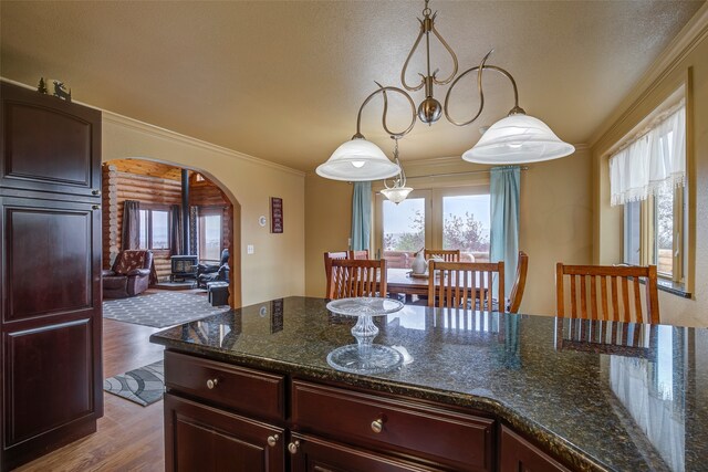 kitchen featuring dark stone countertops, ornamental molding, pendant lighting, and light hardwood / wood-style flooring